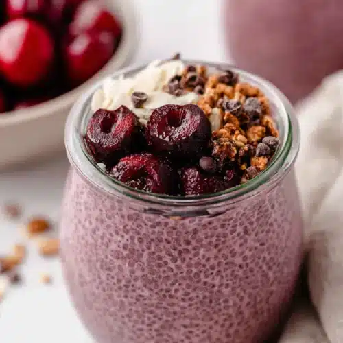 Cherry chia pudding topped with granola and cherries in a glass jar