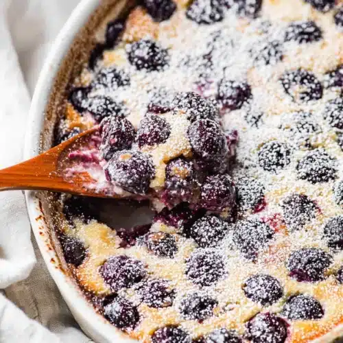 Cherry Clafoutis Recipe: Easy, Custardy French Dessert 4 Cherry clafoutis with powdered sugar and juicy cherries in a rustic baking dish