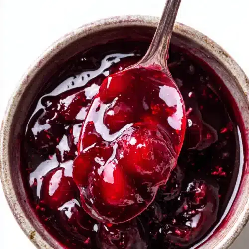 Cherry Syrup Recipe Easy, Sweet, and Irresistible 3 Thick homemade cherry syrup with spoon in bowl, glossy red fruit sauce