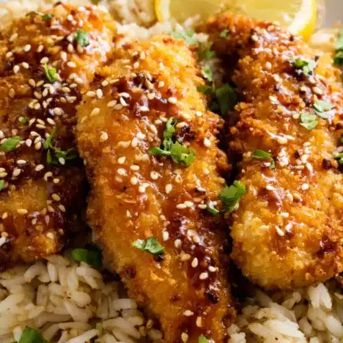 Crunchy hot honey chicken with sesame seeds served over rice with lemon wedge