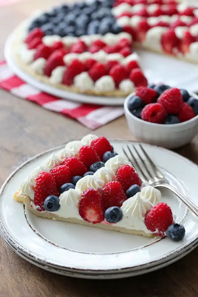 Easy American Flag Fruit Pizza slice with berries and cream on a white plate