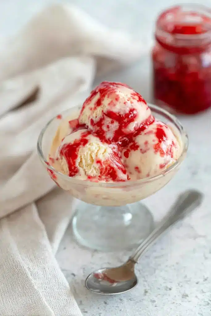 Rhubarb ice cream with red fruit sauce served in glass dessert bowl