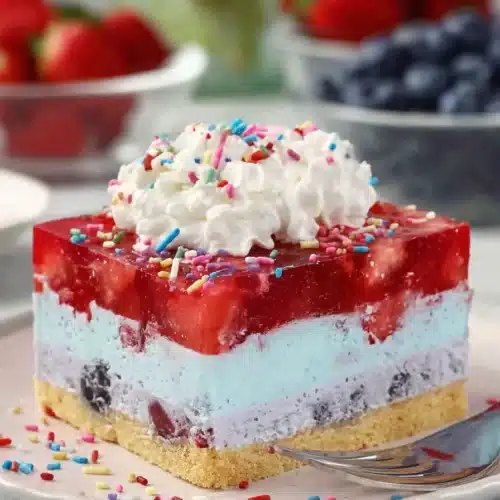 Summer berry jello lasagna slice with whipped cream and fresh strawberries on a plate