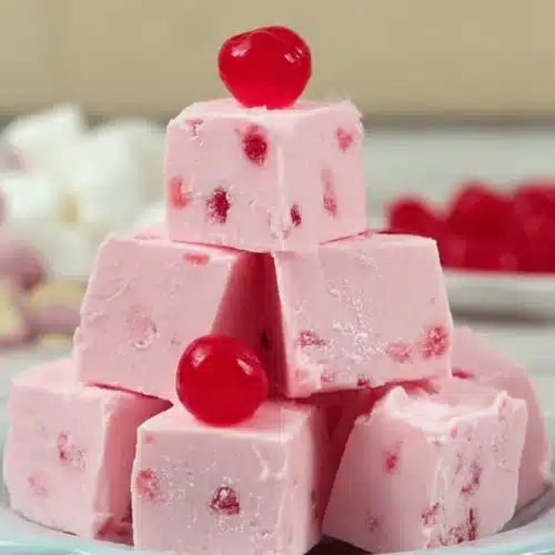 Pink white chocolate cherry fudge cubes stacked with glossy cherry on top