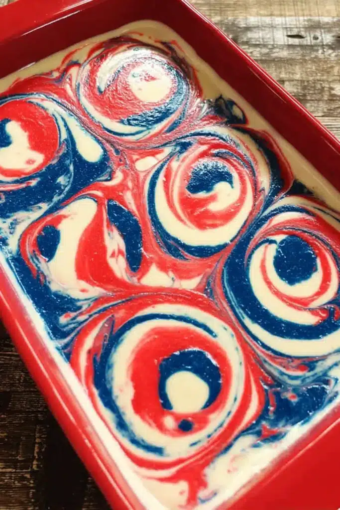 Patriotic Poke Cake batter with red white and blue swirls in baking dish