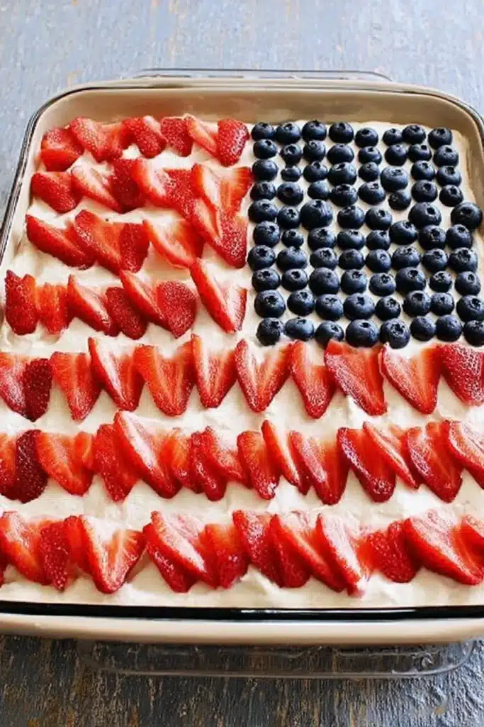 American Flag Strawberry Poke Cake decorated with strawberries and blueberries