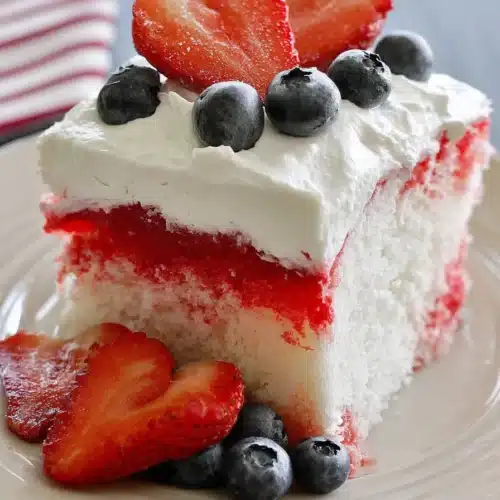 American Flag Strawberry Poke Cake slice topped with strawberries and blueberries