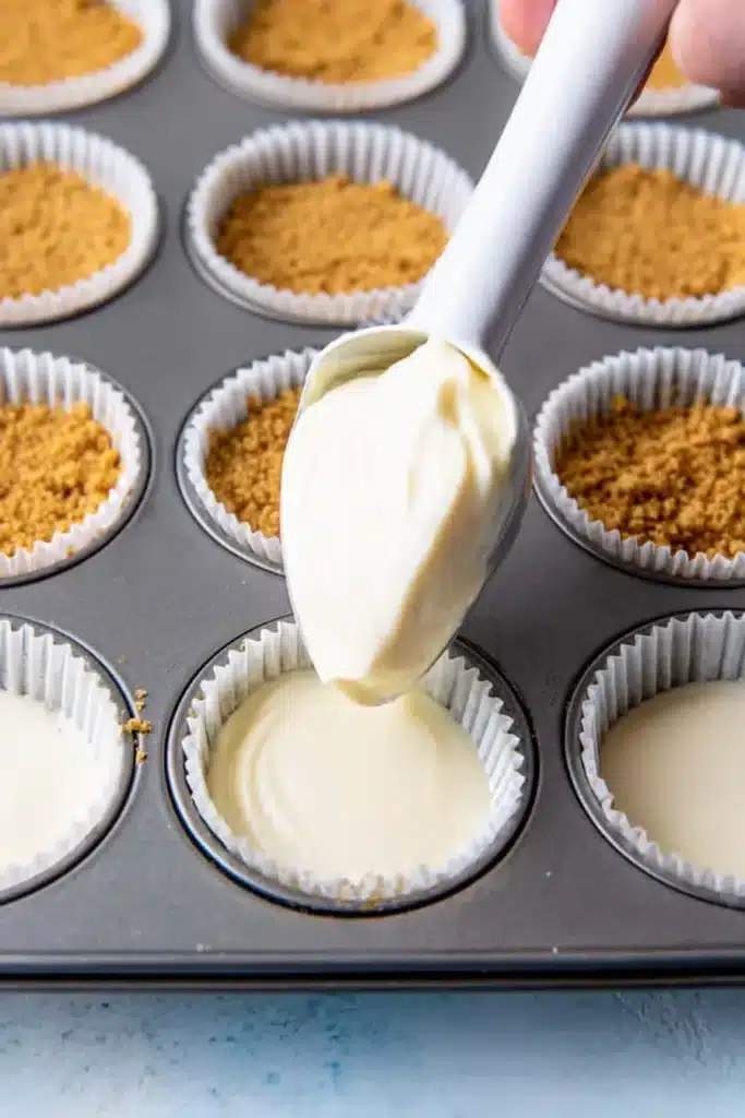 Mini Cheesecake Cups 2 Mini Cheesecake Cups batter being scooped into muffin liners over graham cracker crust