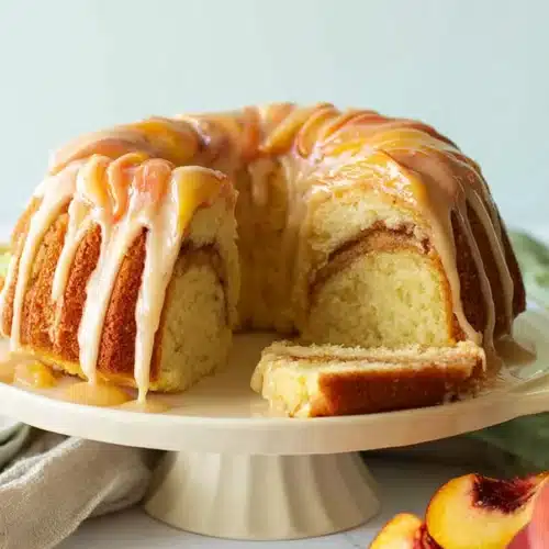 Peach cobbler pound cake with glaze on a cake stand and fresh peaches