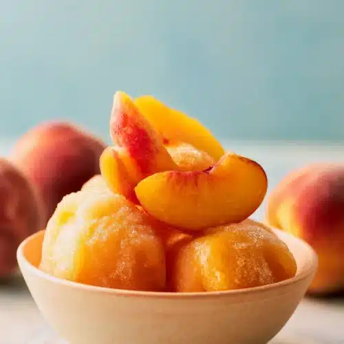 Peach Sorbet 6 Peach Sorbet scoops in a ceramic bowl with fresh peach slices