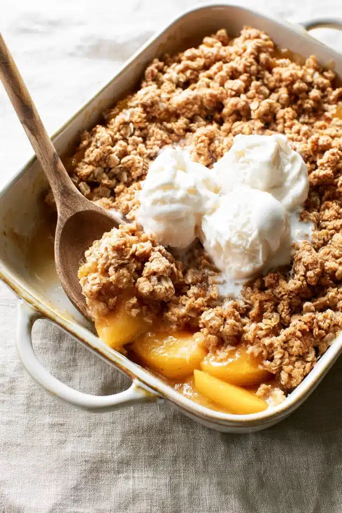 Peach crisp with canned peaches topped with melting vanilla ice cream in a baking dish