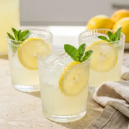 Three Ingredient Homemade Lemonade 5 Three ingredient homemade lemonade in tall glasses with lemon slices, mint, and ice on a wooden board